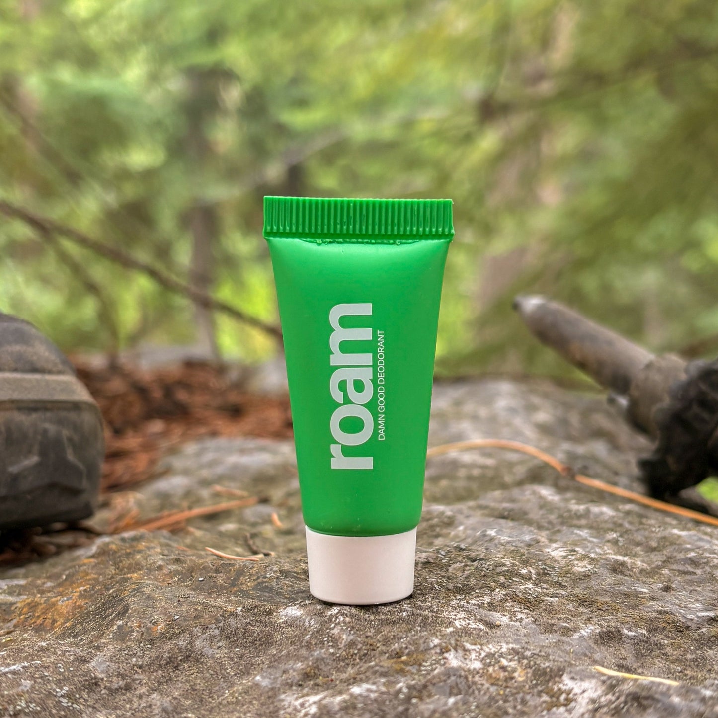 Green tube of 'roam' deodorant on a rock with hiking boots and nature in the background