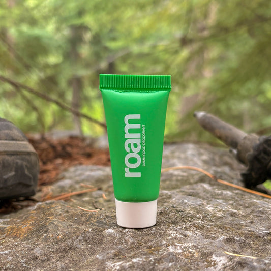 Green tube of 'roam' deodorant on a rock with hiking boots and nature in the background