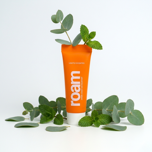 Orange tube of 'roam' product with green leaves on a white background